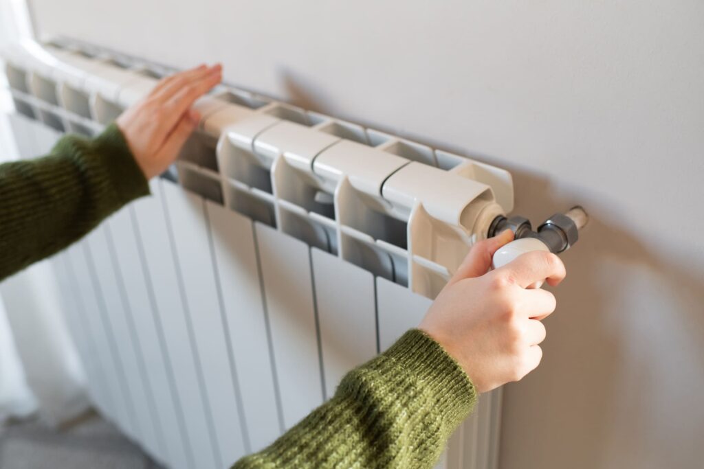 Heizpflicht für Vermieter: Zwei Hände an einer Heizung, die rechte Hand dreht am Knopf.
